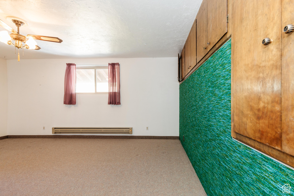 Carpeted spare room with ceiling fan, baseboard heating, and a textured ceiling