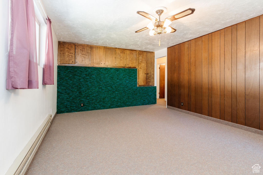 Carpeted spare room featuring ceiling fan, a textured ceiling, wood walls, and a baseboard heating unit