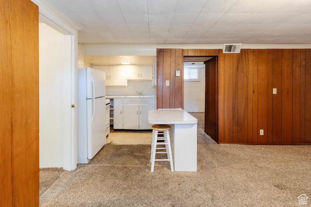 Kitchen featuring white cabinetry, wood walls, a breakfast bar area, white fridge, and light carpet