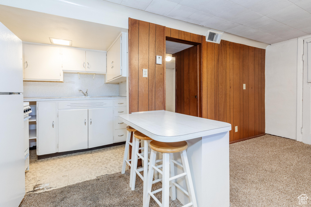 Kitchen featuring white refrigerator, a breakfast bar, wood walls, and white cabinetry