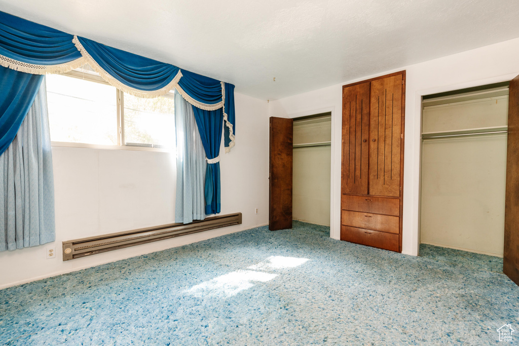 Unfurnished bedroom featuring carpet floors, a closet, and a baseboard heating unit