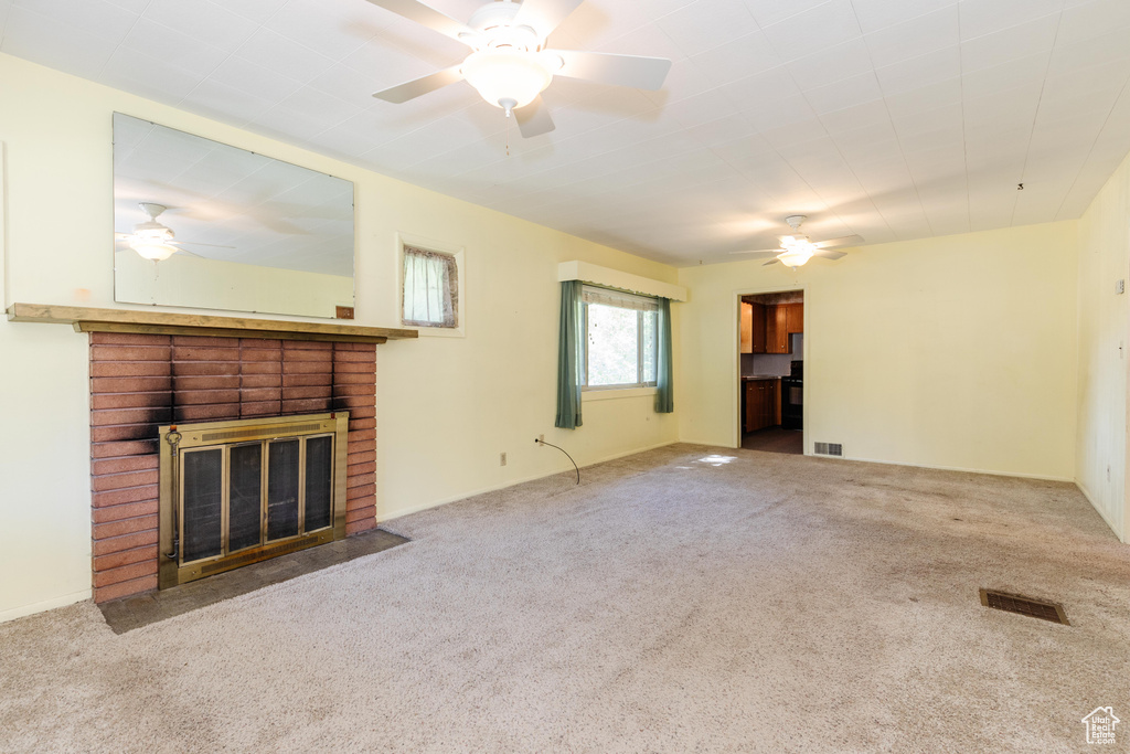 Unfurnished living room featuring carpet, ceiling fan, and a brick fireplace