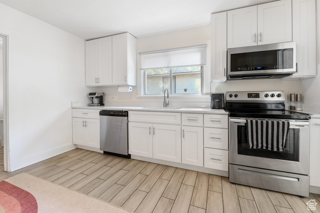 Kitchen featuring light wood-type flooring, sink, stainless steel appliances, and white cabinets