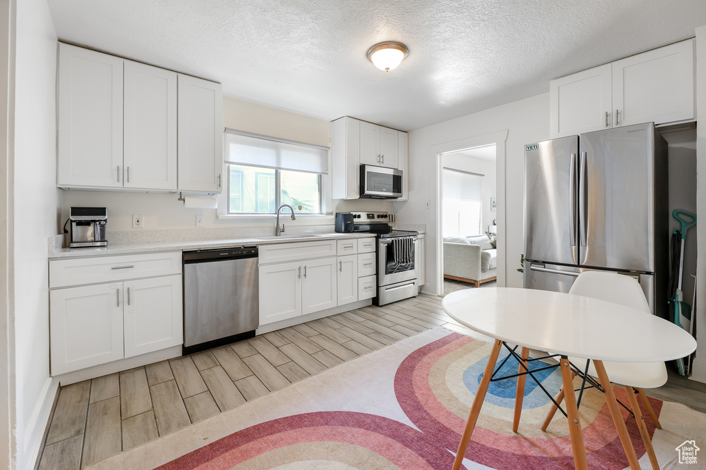 Kitchen featuring white cabinets, stainless steel appliances, light wood-type flooring, a textured ceiling, and sink