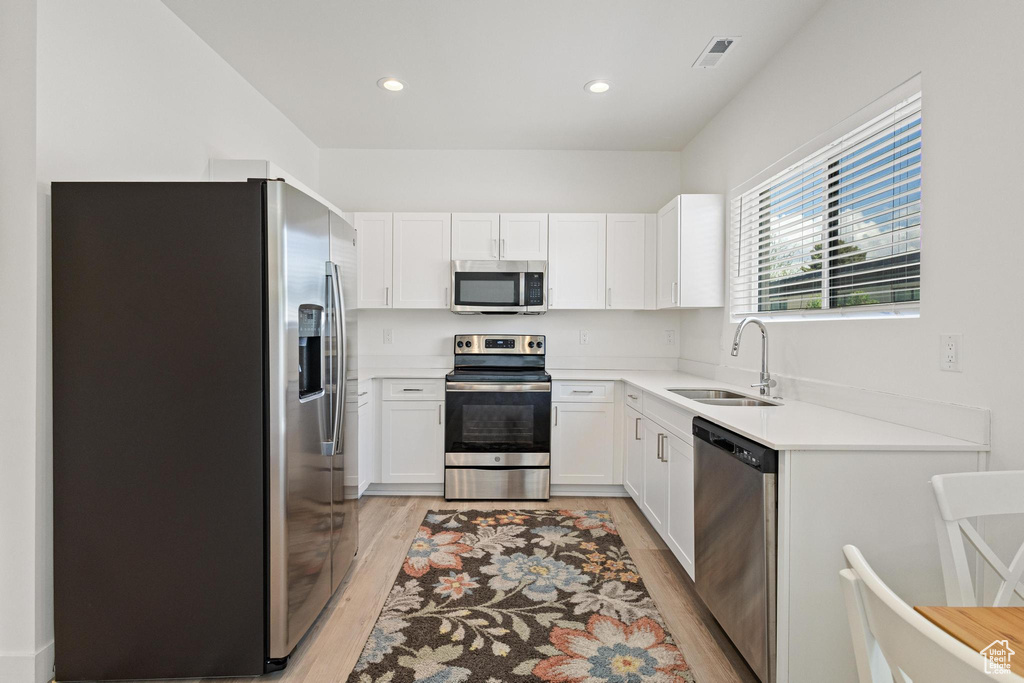 Kitchen with white cabinets, a sink, light countertops, stainless steel appliances, and light wood-type flooring