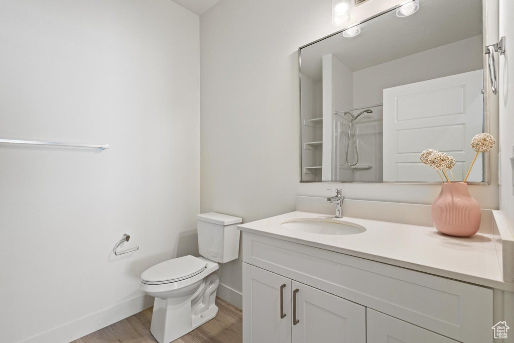 Bathroom with walk in shower, wood finished floors, vanity, baseboards, and toilet