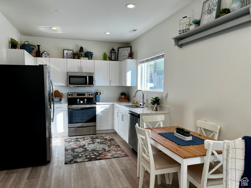 Kitchen featuring appliances with stainless steel finishes, white cabinetry, sink, and light hardwood / wood-style flooring