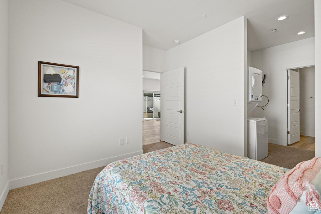 Bedroom with baseboards, recessed lighting, stacked washer / drying machine, and light carpet