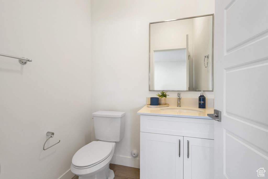 Half bath featuring vanity, baseboards, toilet, and wood finished floors