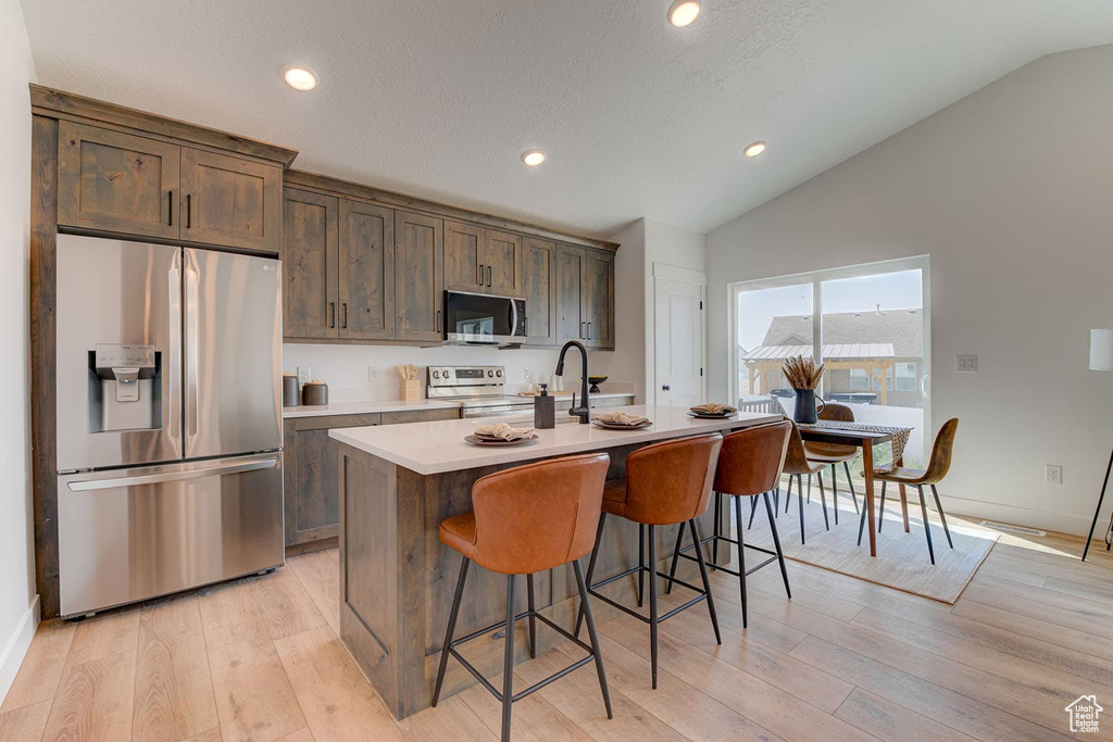 Kitchen with lofted ceiling, a kitchen island with sink, light hardwood / wood-style flooring, stainless steel appliances, and a kitchen breakfast bar