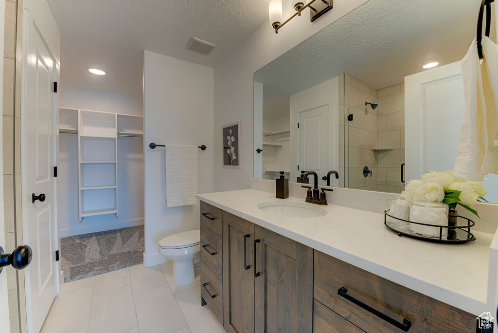 Bathroom featuring a tile shower, a textured ceiling, tile patterned floors, vanity, and toilet