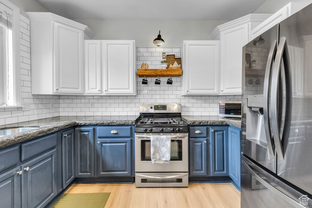 Kitchen with blue cabinetry, white cabinets, stainless steel appliances, and light hardwood / wood-style floors