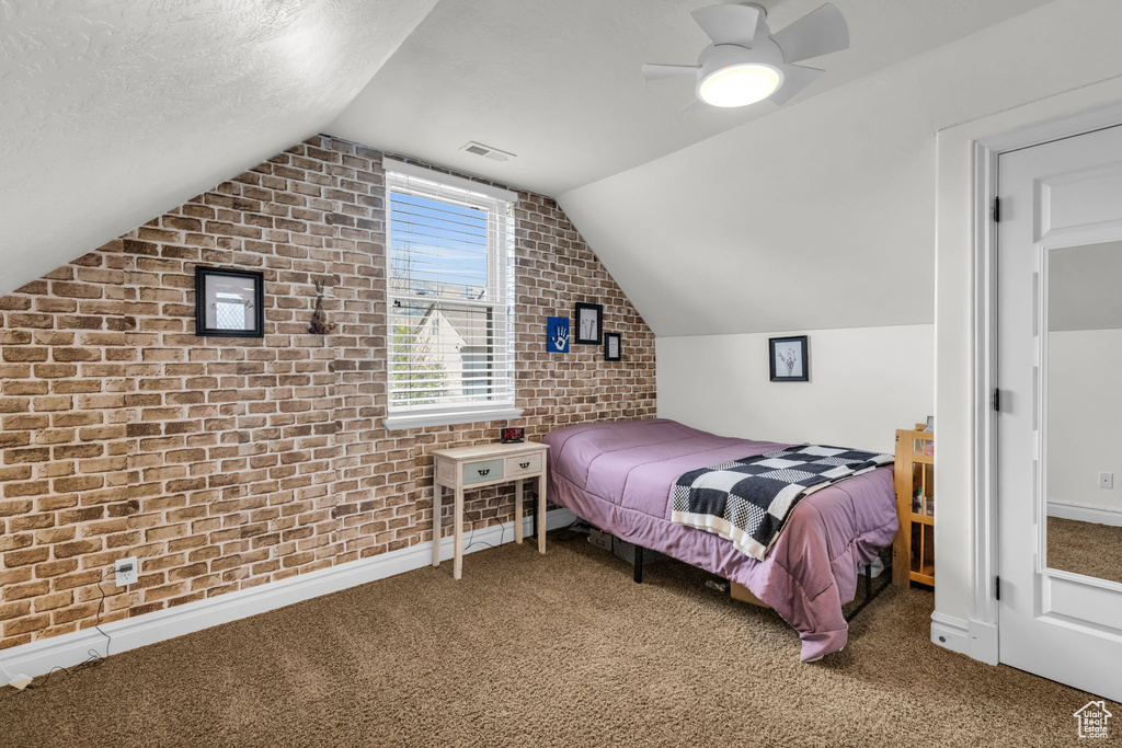 Carpeted bedroom featuring a textured ceiling, lofted ceiling, ceiling fan, and brick wall