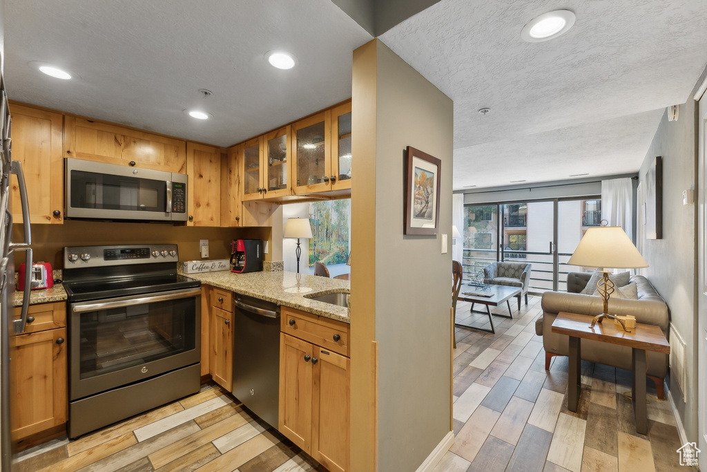 Kitchen with light stone countertops, light hardwood / wood-style floors, appliances with stainless steel finishes, and a textured ceiling