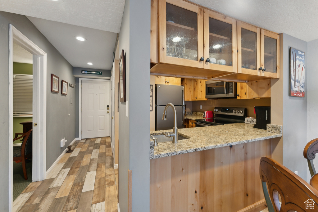 Kitchen with light stone counters, light hardwood / wood-style floors, sink, kitchen peninsula, and appliances with stainless steel finishes