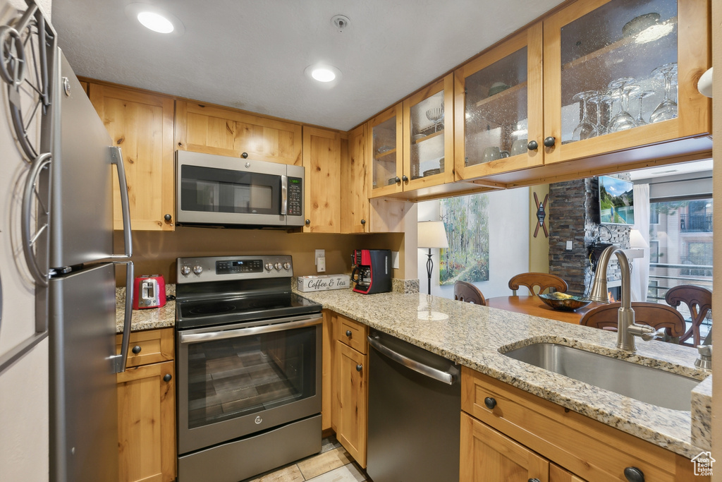 Kitchen with light stone countertops, appliances with stainless steel finishes, sink, and kitchen peninsula