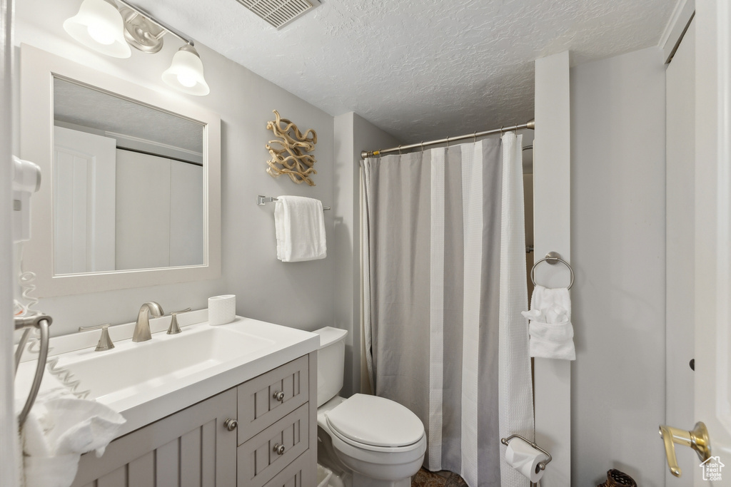 Bathroom with a textured ceiling, curtained shower, vanity, and toilet