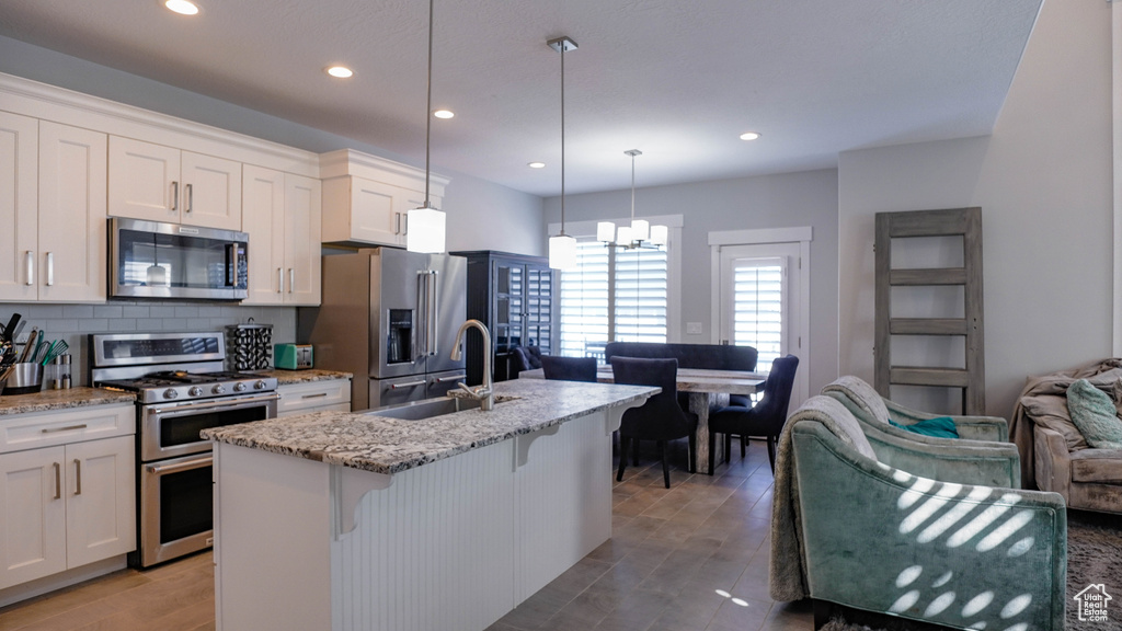 Kitchen featuring appliances with stainless steel finishes, a center island with sink, sink, and white cabinets