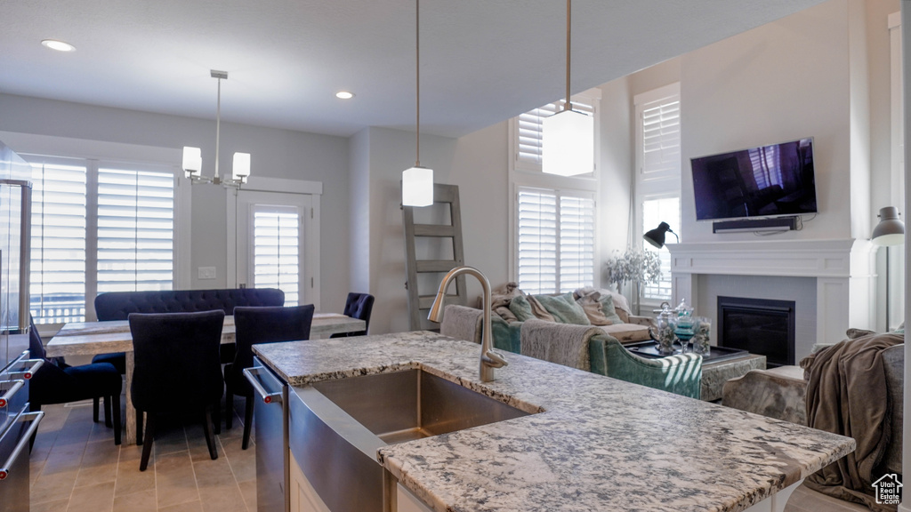 Kitchen with pendant lighting, an island with sink, sink, an inviting chandelier, and light stone countertops