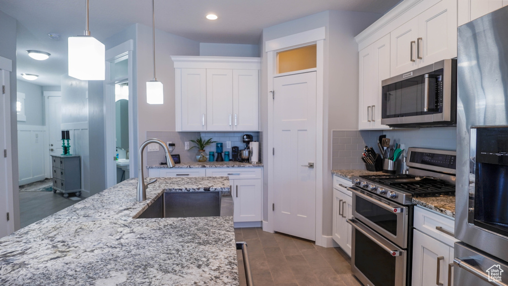 Kitchen with appliances with stainless steel finishes, decorative backsplash, white cabinetry, pendant lighting, and sink