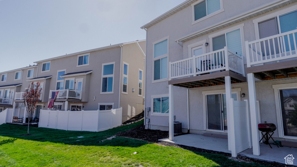 Rear view of house with a balcony, cooling unit, a patio area, and a lawn