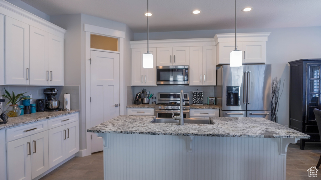 Kitchen featuring high end appliances, white cabinetry, decorative light fixtures, and sink