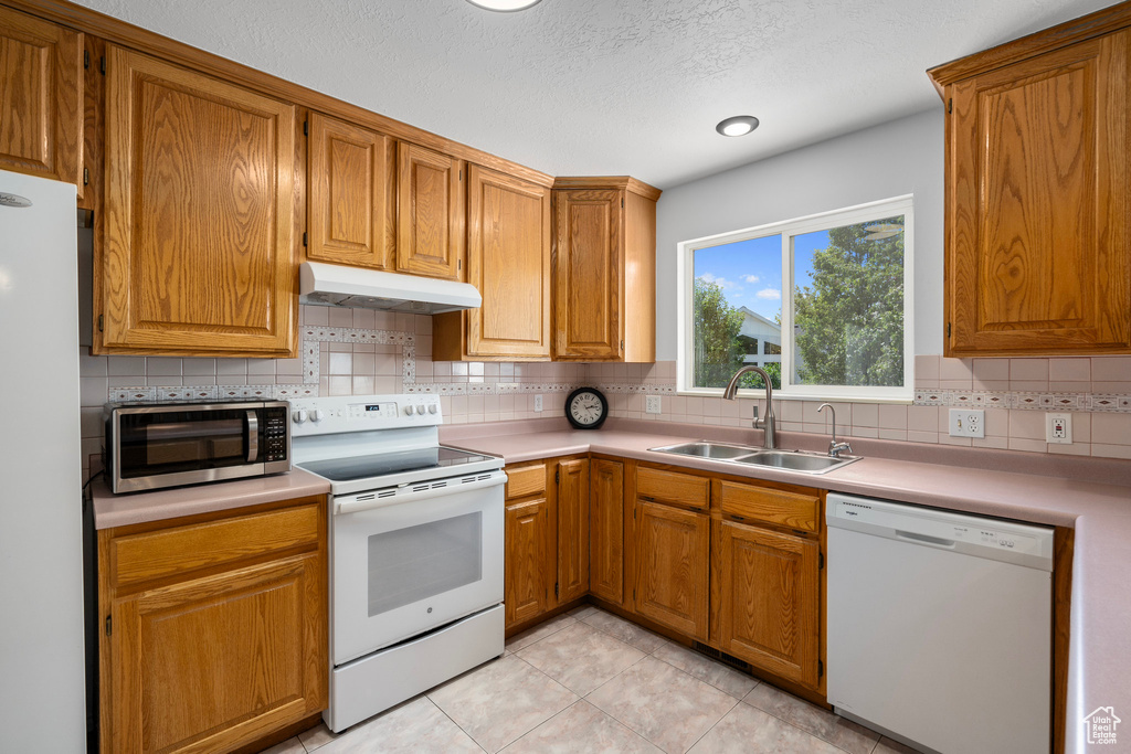 Kitchen featuring a textured ceiling, backsplash, sink, and white appliances