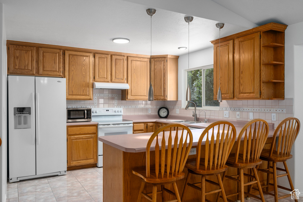 Kitchen with hanging light fixtures, tasteful backsplash, white appliances, kitchen peninsula, and sink