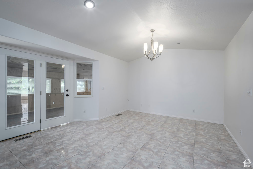 Tiled spare room with a notable chandelier, lofted ceiling, and a healthy amount of sunlight