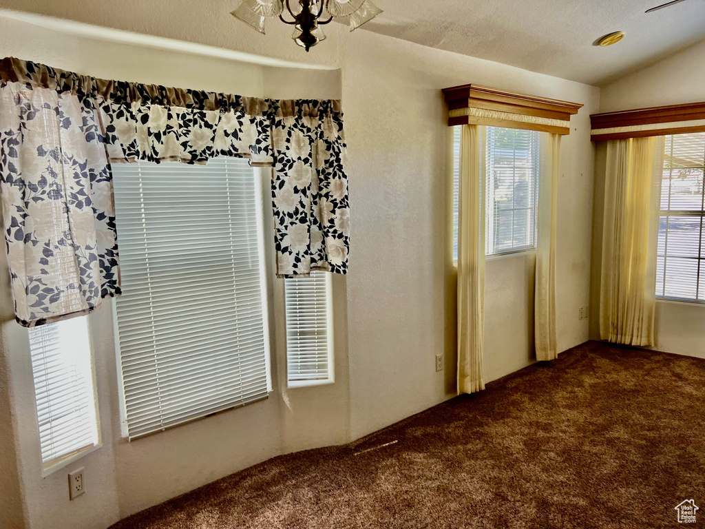 Carpeted spare room with lofted ceiling, a chandelier, a textured ceiling, and plenty of natural light