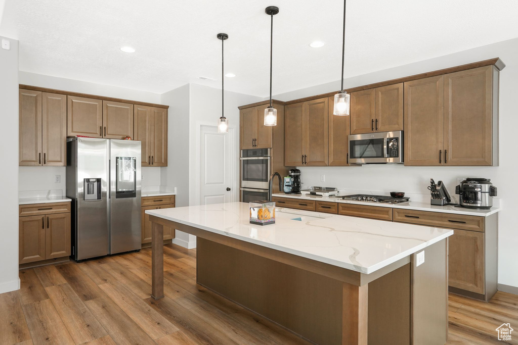 Kitchen with sink, decorative light fixtures, stainless steel appliances, a center island, and light hardwood / wood-style floors