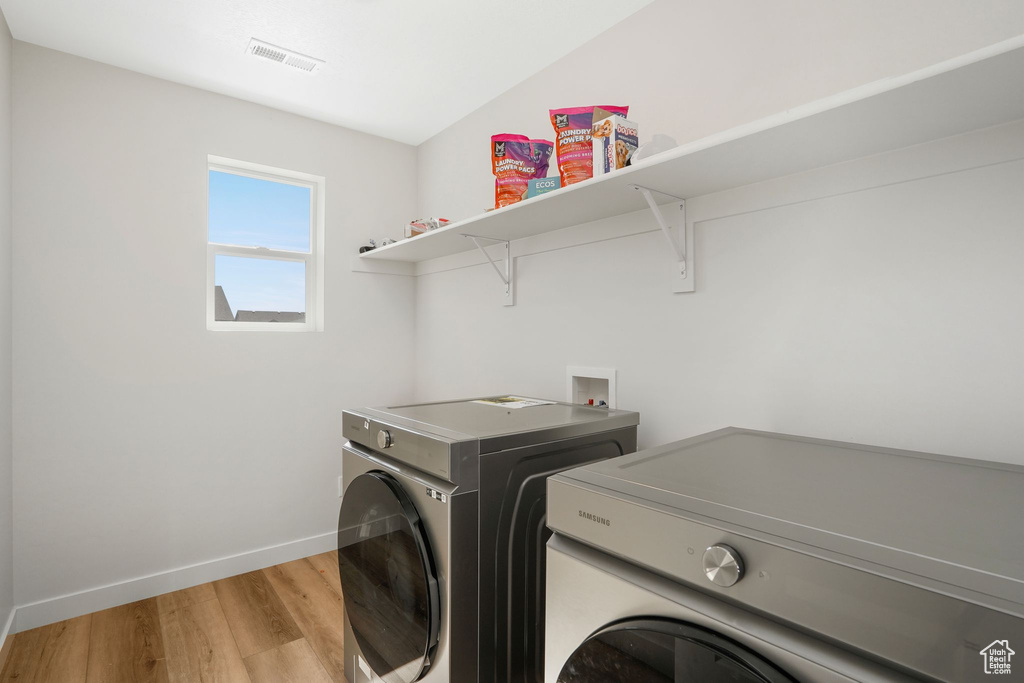 Laundry area with light hardwood / wood-style floors and washing machine and clothes dryer