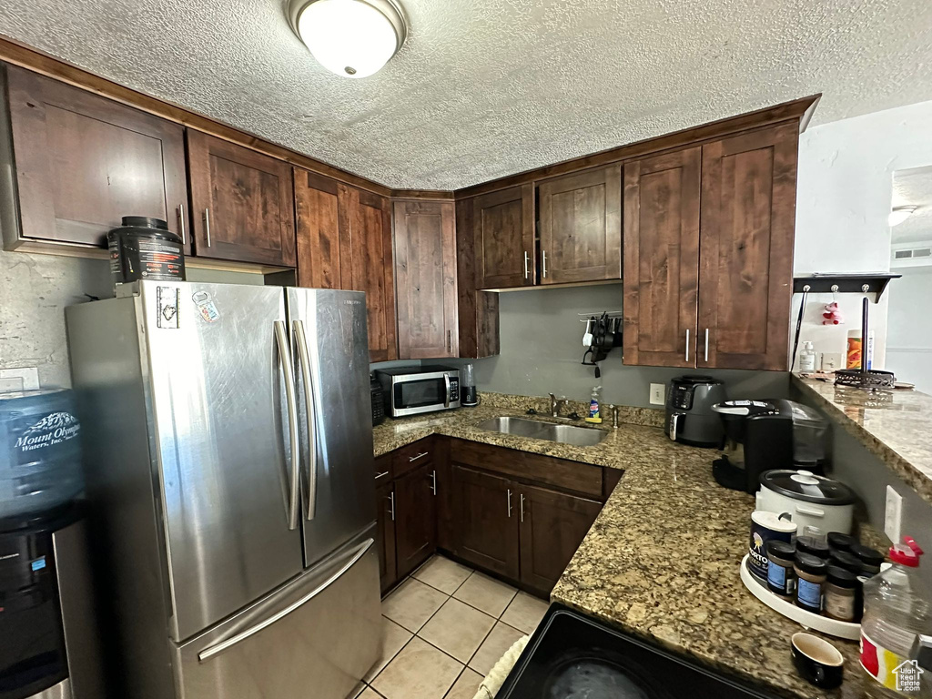 Kitchen with sink, dark brown cabinets, a textured ceiling, stainless steel appliances, and light stone countertops