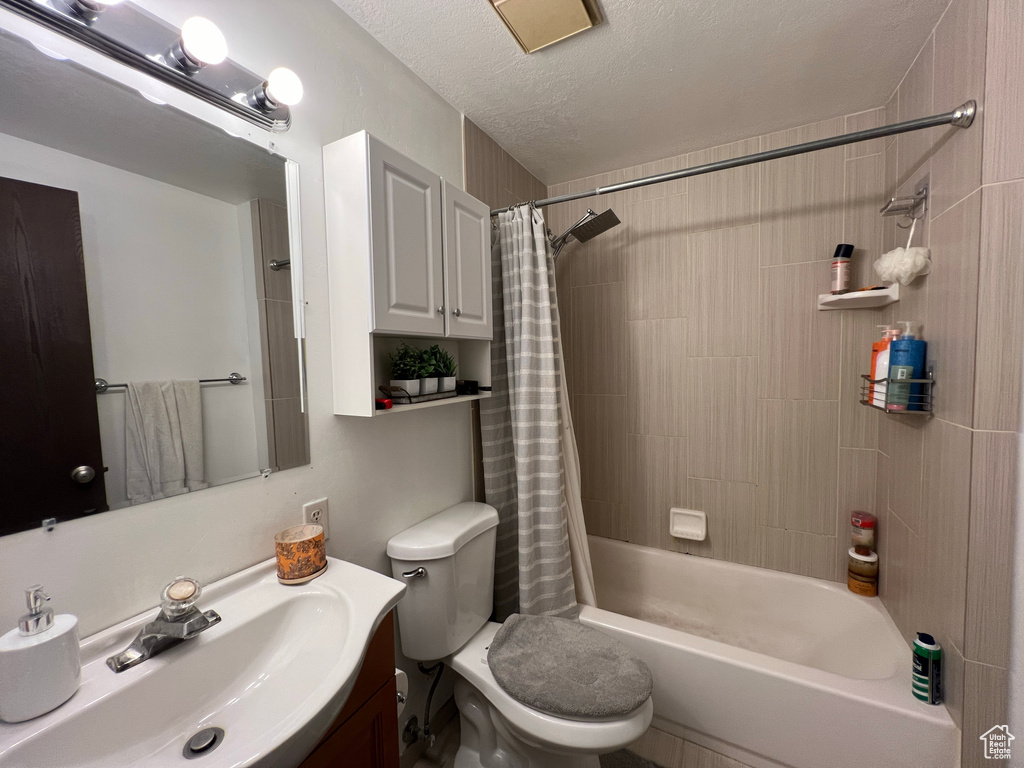 Full bathroom featuring shower / bath combination with curtain, a textured ceiling, vanity, and toilet