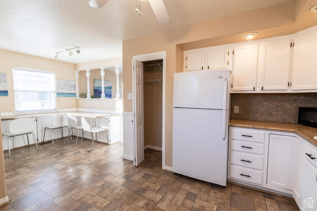 Kitchen with white cabinets, ceiling fan, white fridge, and tasteful backsplash