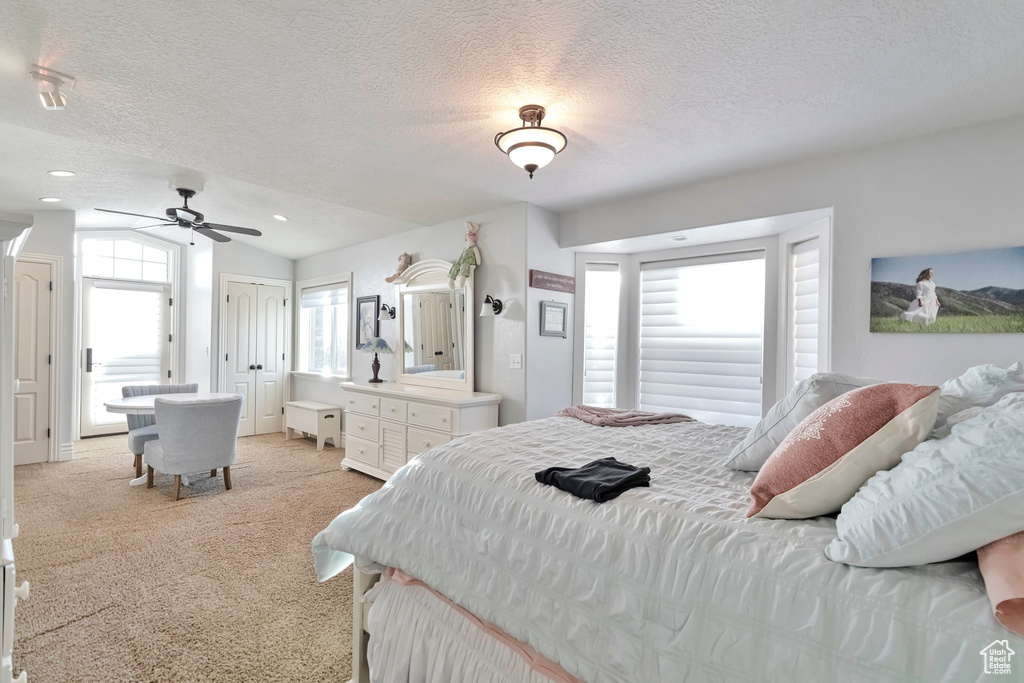 Carpeted bedroom with ceiling fan, a textured ceiling, vaulted ceiling, and multiple windows