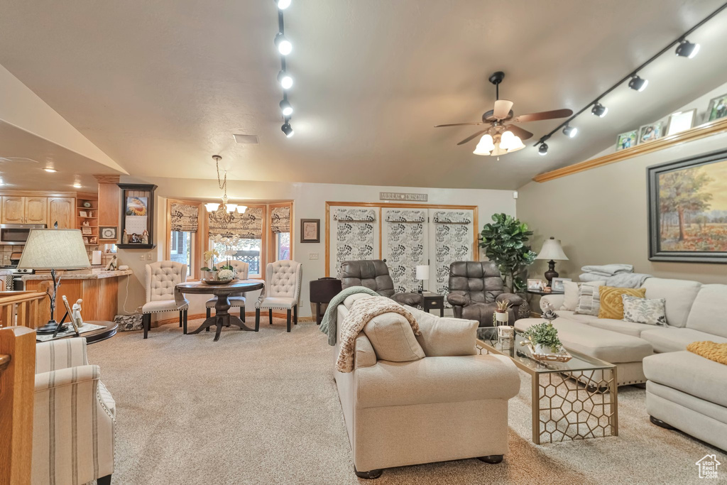 Carpeted living room with ceiling fan with notable chandelier, vaulted ceiling, and rail lighting