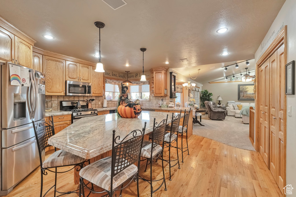 Kitchen with pendant lighting, light hardwood / wood-style flooring, backsplash, stainless steel appliances, and vaulted ceiling