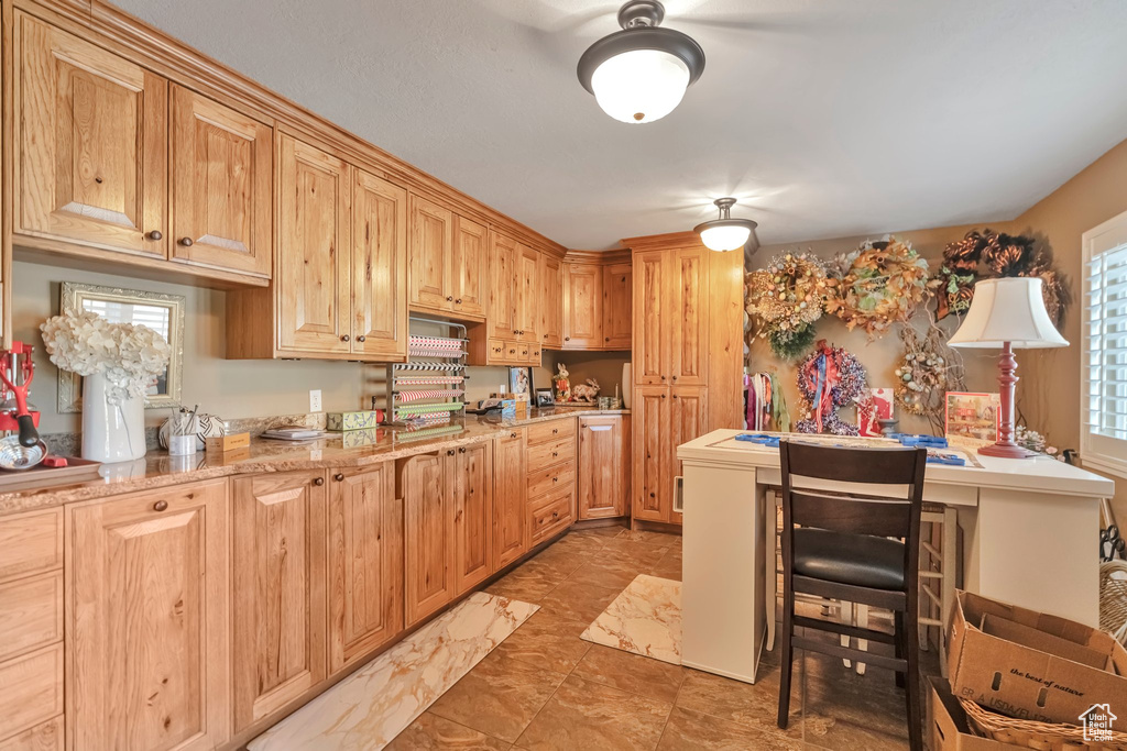 Kitchen with light stone counters, light brown cabinets, a breakfast bar, and a healthy amount of sunlight