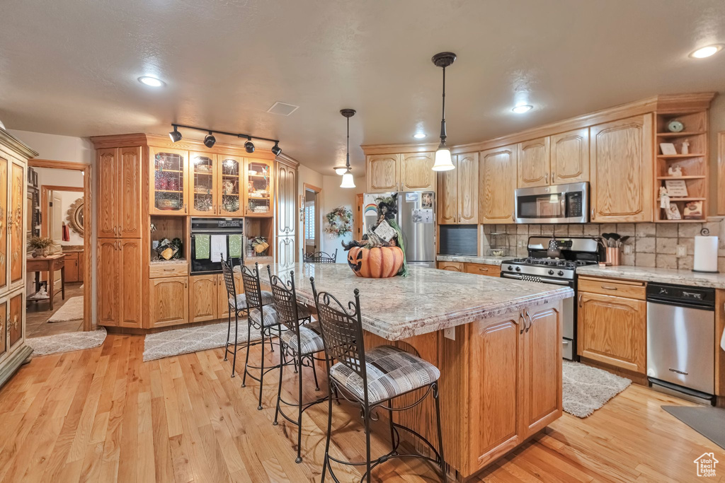 Kitchen featuring a kitchen island, stainless steel appliances, hanging light fixtures, and light hardwood / wood-style flooring