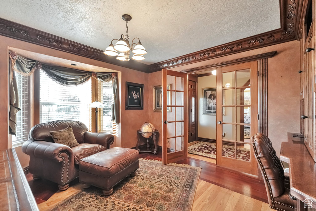 Living room featuring a textured ceiling, light hardwood / wood-style floors, ornamental molding, and french doors