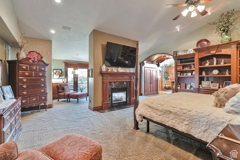 Carpeted bedroom featuring vaulted ceiling, ceiling fan, a fireplace, and a textured ceiling