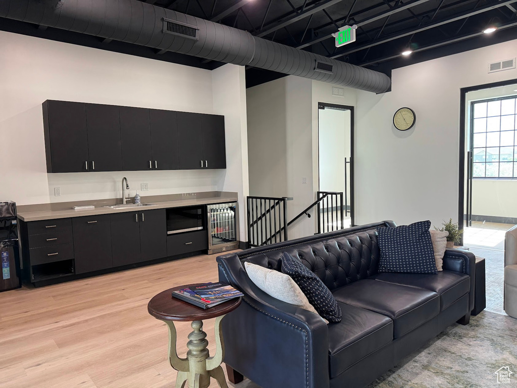 Living room featuring beverage cooler, light wood-style floors, and bar with sink