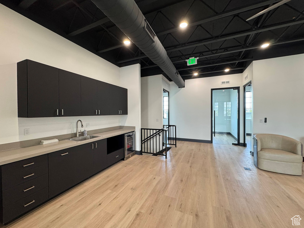 Kitchen with dark cabinets, a sink, light countertops, and beverage cooler