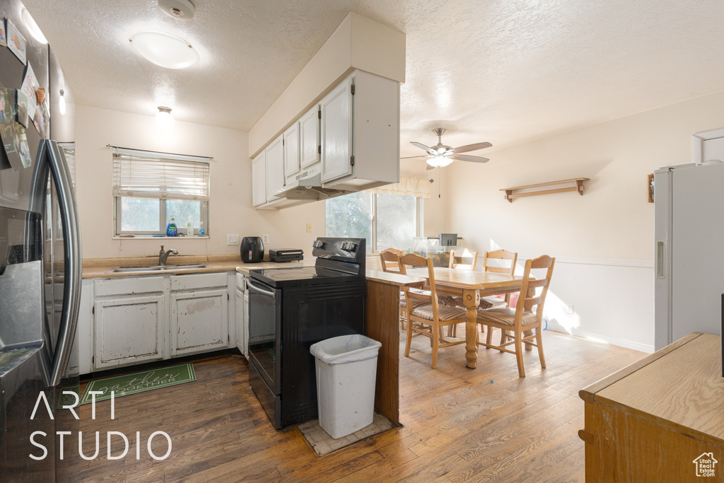 Kitchen featuring stainless steel fridge, dark hardwood / wood-style floors, black range with electric stovetop, and a wealth of natural light