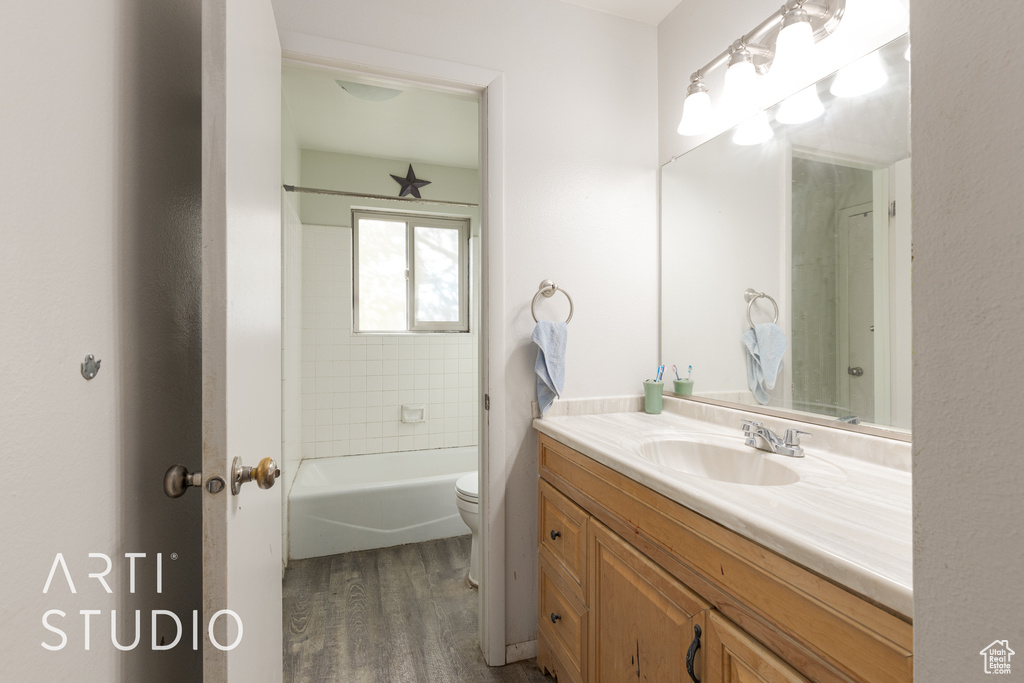 Full bathroom featuring wood-type flooring, tiled shower / bath, vanity, and toilet