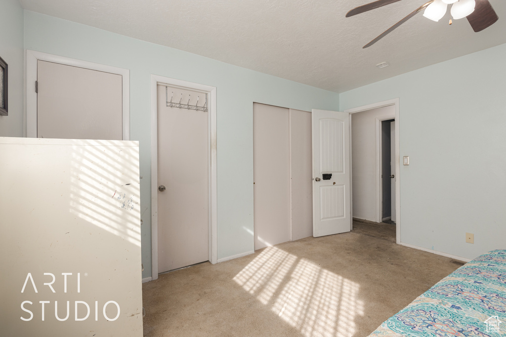 Unfurnished bedroom featuring a textured ceiling, light carpet, and ceiling fan