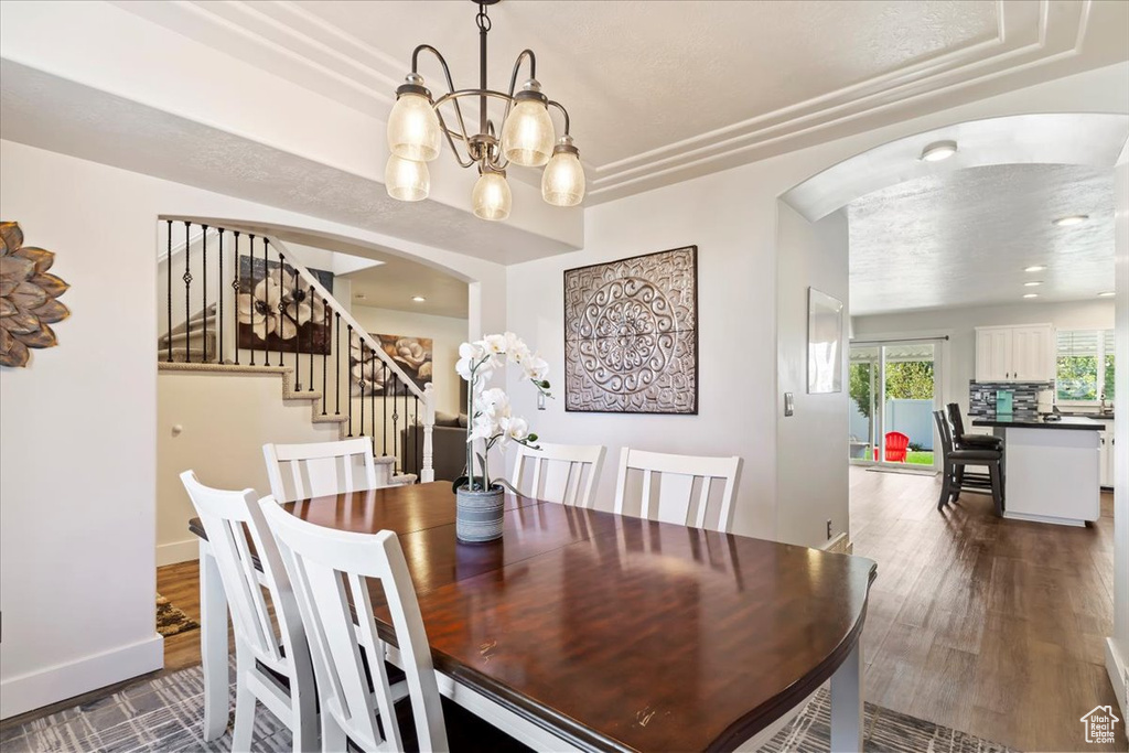 Dining room with a textured ceiling, a raised ceiling, dark hardwood / wood-style floors, and a notable chandelier