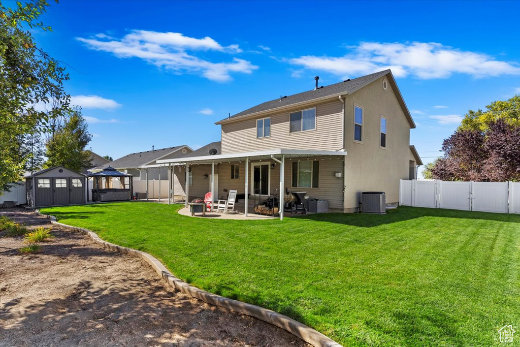 Rear view of house featuring a patio, cooling unit, a storage shed, and a lawn