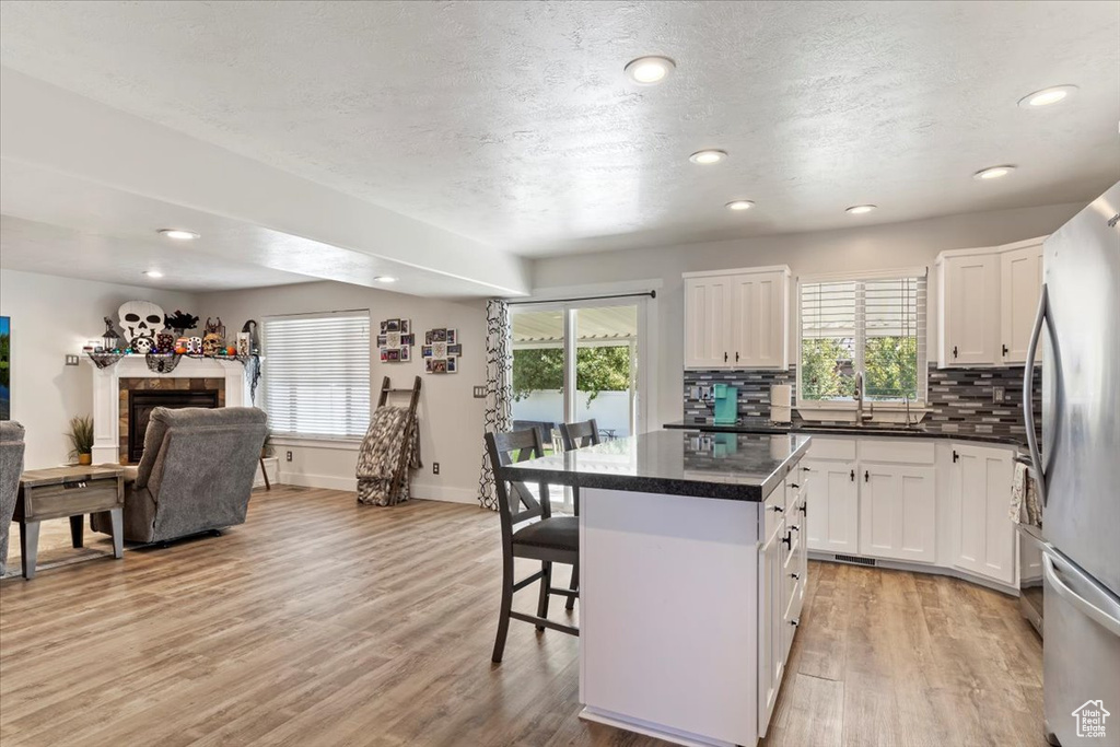 Kitchen with a tile fireplace, white cabinets, a kitchen island, light hardwood / wood-style flooring, and a kitchen breakfast bar